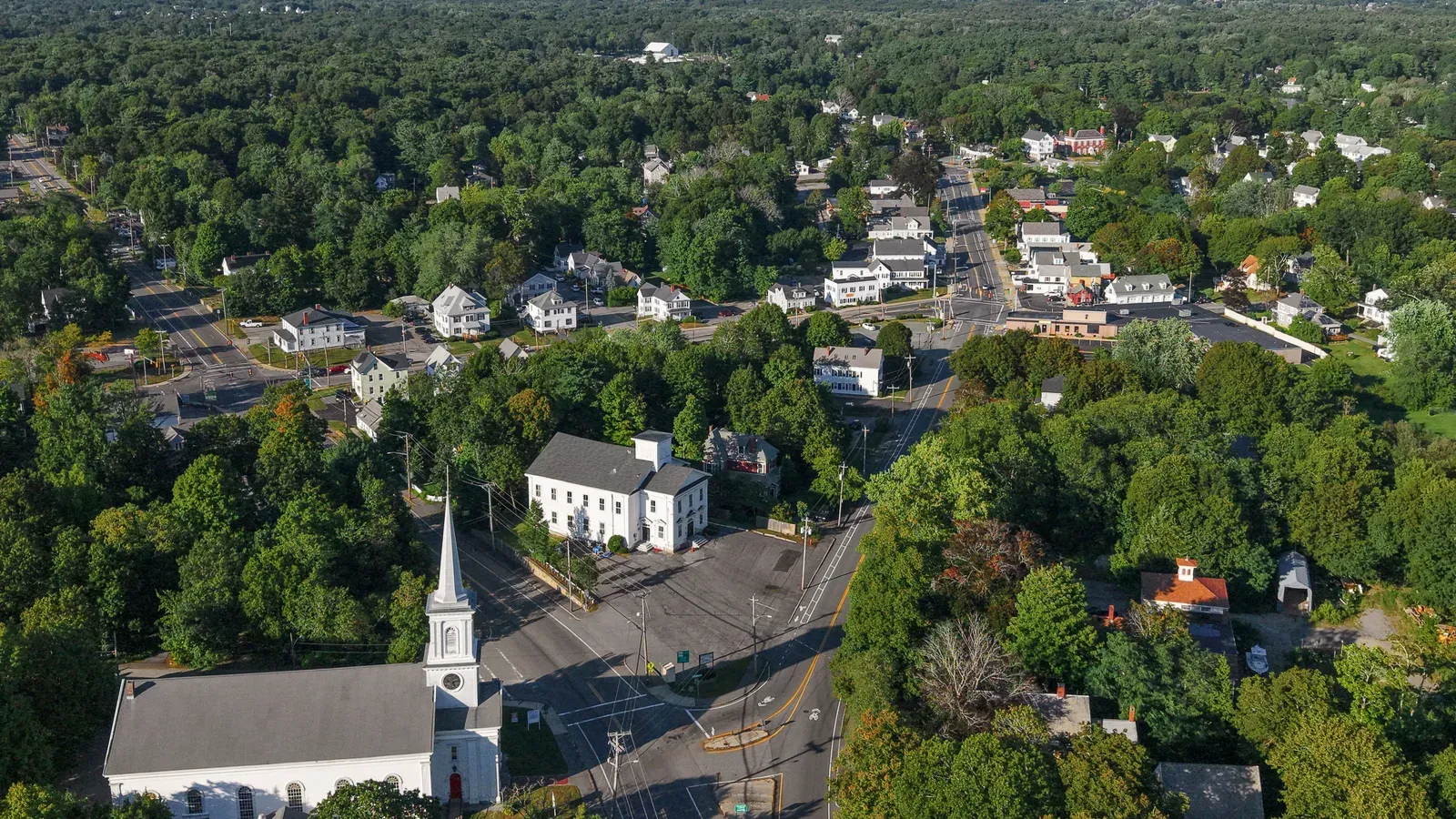 Aerial view over Abington center, a white-steepled church and colonial homes set among dense tree canopy, Abington, Massachusetts