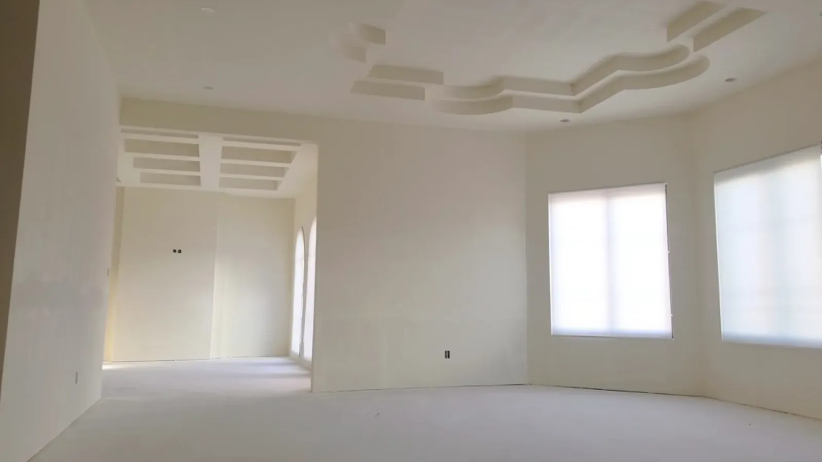 An open interior skim-coated throughout to a smooth uniform finish, with a stepped tray ceiling and plastic-masked windows