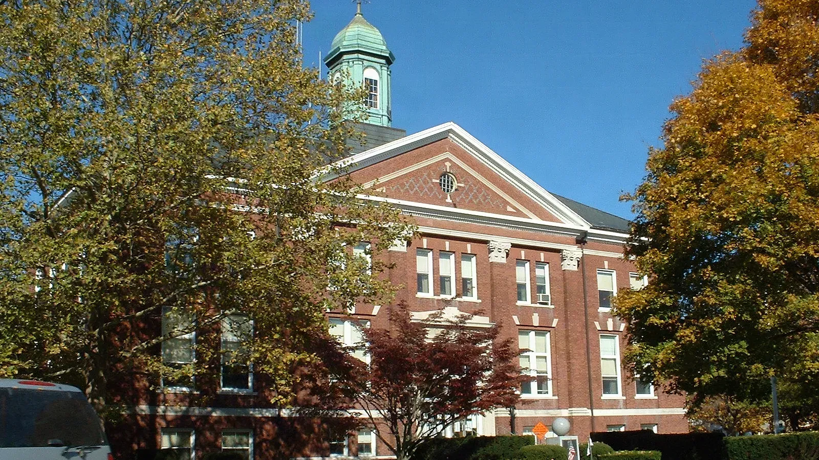 Whitman Town Hall, a Georgian Revival red-brick building with a white pediment and green copper cupola among autumn trees, Whitman, Massachusetts